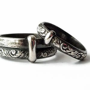 May include: Two silver rings with ornate floral patterns and a dark, oxidized finish. One ring is stacked on top of another, with a third ring resting beside them. The rings have a vintage, gothic aesthetic.