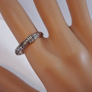 May include: A silver ring with an engraved floral pattern and a decorative band. The ring is on a finger, showcasing the intricate details of the design. The ring's band is approximately 0.25 inches wide.