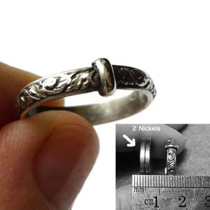 May include: A silver ring with an ornate floral design and a central bar. The ring is held in a hand, with a close-up showing the details. The ring's width is shown next to a ruler, with the text "2 Nickels".