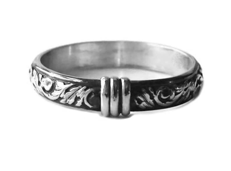 May include: A silver ring with an ornate, floral design. The ring features a dark, oxidized finish on the outer band, with a detailed pattern of swirling leaves and flowers. The ring has a unique, raised section with three vertical bars.