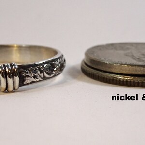 May include: A silver ring with an engraved floral pattern and a decorative band. The ring is next to a nickel and a quarter for size comparison. The text "nickel & quarter" is below the coins.