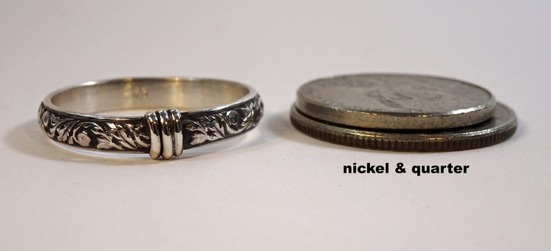 May include: A silver ring with an engraved floral pattern and a decorative band. The ring is next to a nickel and a quarter for size comparison. The text "nickel & quarter" is below the coins.