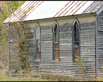 May include: A weathered wooden building with three arched windows. The building has a rusty metal roof and is painted a faded gray color.
