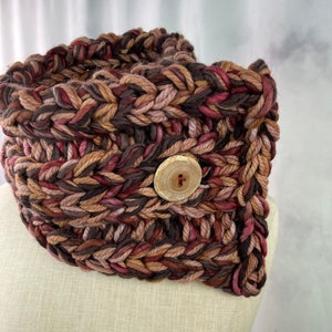 May include: A brown, pink, and black crocheted neck warmer with a wooden button.