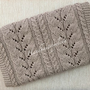 May include: A brown knitted blanket with a cable knit pattern. The blanket is made with a soft yarn and has a delicate, lacy look.