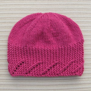 May include: A pink knitted hat with a decorative stitch pattern around the brim.