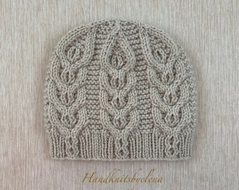 May include: A light beige knit beanie featuring a vertical cable knit pattern with repeating leaf-like motifs and a ribbed brim. The hat is constructed with a textured stitch design and includes the text Handknitsbyelena at the bottom.