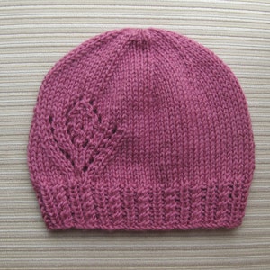 May include: A pink knitted hat with a lacy pattern. The hat is made of soft yarn and has a simple, classic design.
