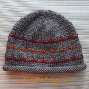 May include: A gray knit beanie with red and orange leaf-like patterns. The hat has a folded brim and is made of a soft, textured yarn. The text "Handknits by elena" is visible in the image.