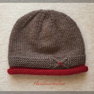 May include: A brown knitted hat with a red brim and a small brown bow with red beads in the centre. The hat is labelled "Handknitsbyelena".