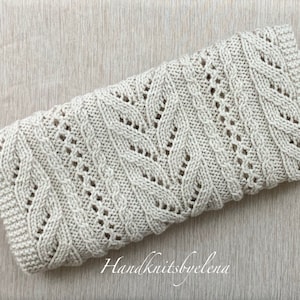 May include: A beige knitted blanket with a cable knit pattern and a delicate lace design. The blanket is folded and lying on a textured beige surface. The text "Handknitsbyelena" is visible in the lower right corner of the image.