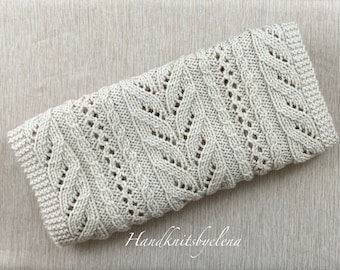 May include: A rectangular, off-white knitted fabric piece featuring a central leaf-like lace pattern flanked by vertical cable stitches and eyelet columns. The edges are finished with a garter stitch border. The text Handknitsbyelena is visible.