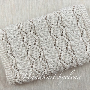 May include: A rectangular, off-white knitted fabric piece featuring a repeating vertical pattern of textured cable stitches interspersed with delicate eyelet lace columns. The text Handknitsbyelena is printed in white script across the lower section.