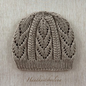 May include: A light brown knitted beanie featuring a repeating vertical leaf-like lace pattern and a ribbed brim. The text Handknitsbyelena is printed in a cursive script at the bottom center of the image.