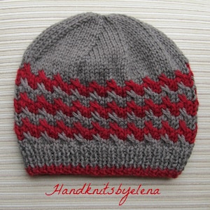 May include: A grey and red knit beanie featuring a textured zigzag pattern across the middle section and a ribbed brim. The text Handknitsbyelena is printed in red cursive script at the bottom of the image, centered below the knit hat.