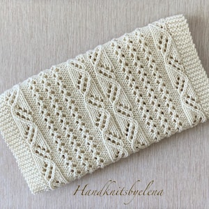 May include: A rectangular off-white knitted piece featuring a complex pattern of vertical cables and eyelet lace stitches. The edges are finished with a garter stitch border. The text Handknitsbyelena is printed in the bottom right corner.