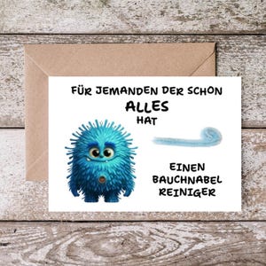 Könnte beinhalten: Eine weiße Grußkarte mit einem blauen, pelzigen, runden Monster mit großen Augen und einem Bauchnabel, daneben ein hellblauer Pfeifenreiniger. Der Text lautet: FÜR JEMANDEN DER SCHON ALLES HAT EINEN BAUCHNABEL REINIGER.