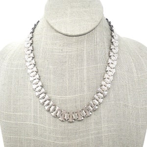 May include: A silver chain necklace with a unique, geometric design. The chain is made up of interlocking links that create a textured, patterned look.