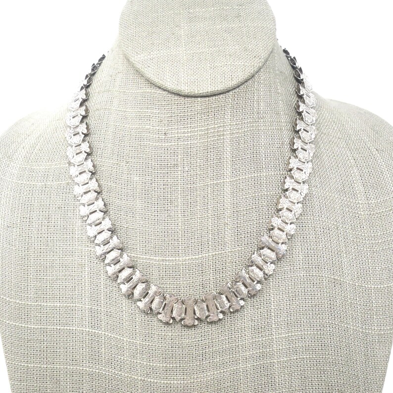 May include: A silver chain necklace with a unique, geometric design. The chain is made up of interlocking links that create a textured, patterned look.