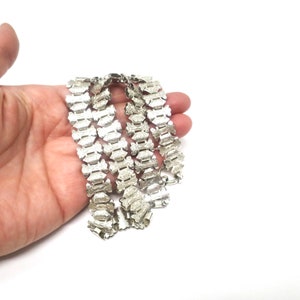 May include: A silver chain necklace with a detailed, intricate design. The chain is made up of small, linked pieces that are shaped like leaves or flowers.