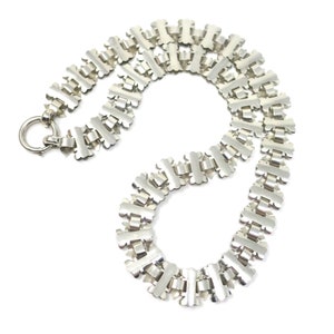 May include: A silver chain necklace with a unique, intricate design. The chain is made up of interlocking links that form a repeating pattern.