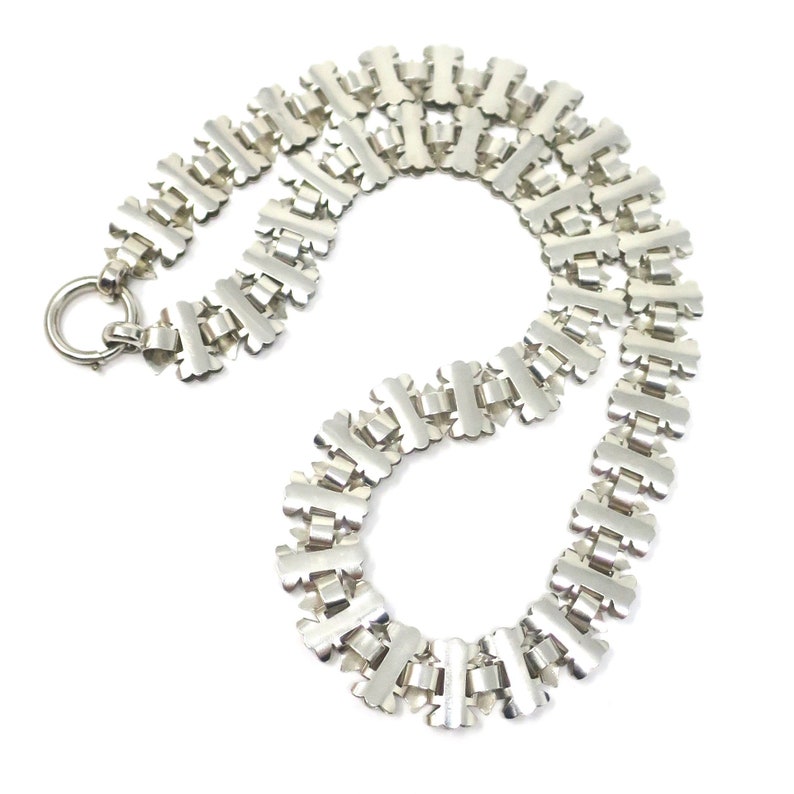 May include: A silver chain necklace with a unique, intricate design. The chain is made up of interlocking links that form a repeating pattern.
