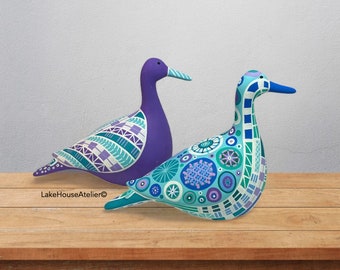 May include: Two duck figurines featuring intricate geometric and circular patterns in shades of purple, teal, blue, and white. The left duck has a solid purple neck and head, while the right duck is covered in detailed blue and teal motifs. LakeHouseAtelier©.