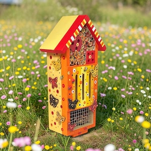 May include: A wooden insect hotel with a yellow and red peaked roof. The structure features a front panel decorated with painted butterflies, ladybugs, and bees. It includes various nesting tubes, a small square compartment, and a wire mesh section.
