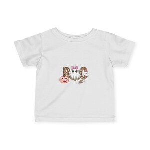 Könnte beinhalten: Ein weißes kurzärmeliges T-Shirt mit einem grafischen Aufdruck des Wortes BOO in Leopardenmuster. Das Design umfasst einen rosa Kürbis, ein weißes Gespenst mit rosa Schleife, ein kleineres Gespenst und eine kleine Spinne unter den Buchstaben.