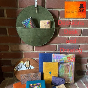 May include: A set of cork and leather desk and drawing accessories in various colors and patterns. The set includes a cork organizer, a teal notebook, a cork and leather pencil holder, and a variety of other items. The text "Decisions Desk and Drawing Set" is visible in the image.