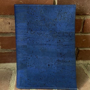May include: A blue cork notebook cover with a subtle speckled pattern. The cover has a stitched edge.