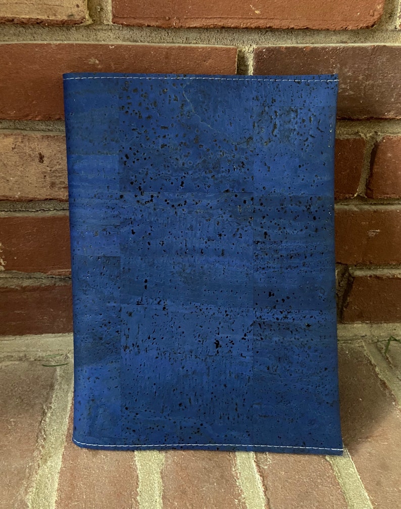 May include: A blue cork notebook cover with a subtle speckled pattern. The cover has a stitched edge.
