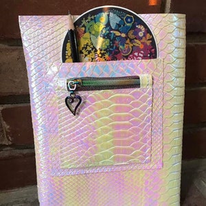 May include: A white iridescent zippered pouch with a snakeskin pattern. The pouch has a small heart charm on the zipper pull. A pencil and a round sticker are inside the pouch.