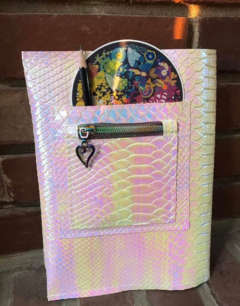 May include: A white iridescent zippered pouch with a snakeskin pattern. The pouch has a small heart charm on the zipper pull. A pencil and a round sticker are inside the pouch.