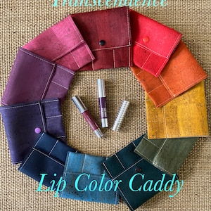 May include: A set of ten cork fabric pouches in various colours, arranged in a circle around two lip glosses and a lip liner. The pouches are labelled "Lip Color Caddy" and "Transcendence".