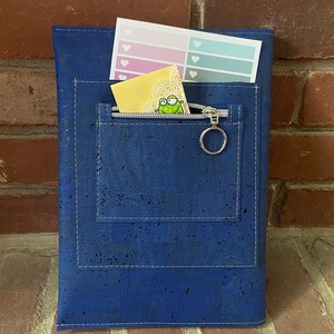 May include: A blue cork notebook with a zippered pocket and a small sticker inside. The notebook has white stitching around the edges.