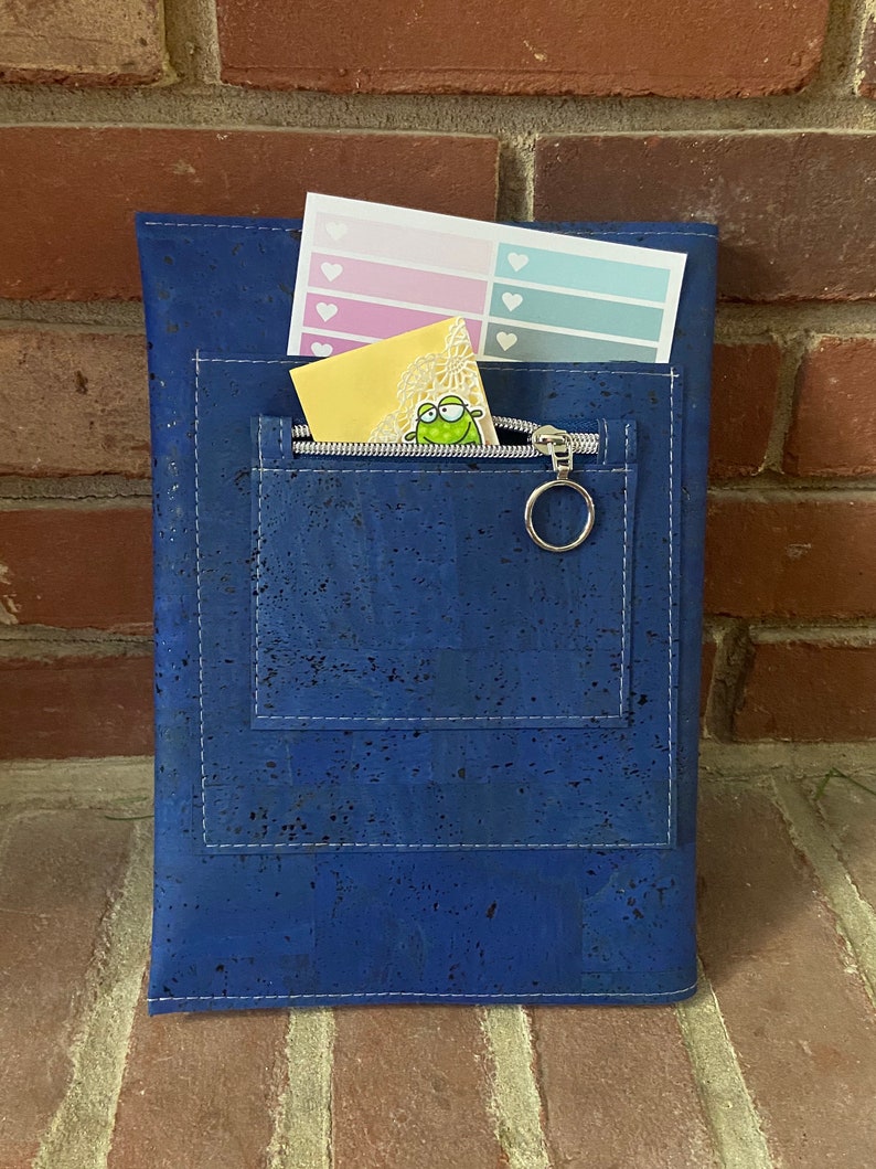 May include: A blue cork notebook with a zippered pocket and a small sticker inside. The notebook has white stitching around the edges.