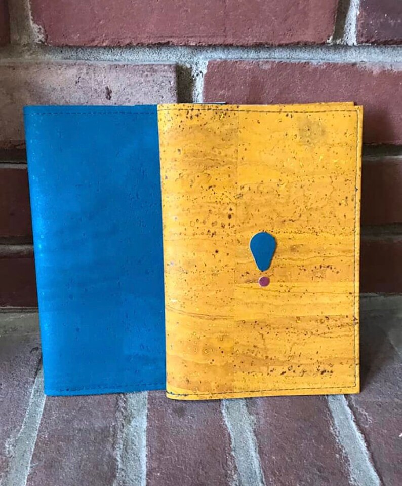 May include: A cork notebook with a blue cover on the left and a yellow cork cover on the right. The yellow cover has a blue and red accent.