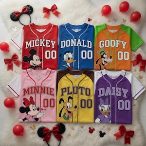 Op de afbeelding: Zes honkbalshirts met Disney-personages Mickey, Donald, Goofy, Minnie, Pluto en Daisy. Elk shirt heeft een karakterafbeelding, een naam en het nummer 00. De shirts zijn rood, blauw, oranje, roze, geel en paars.