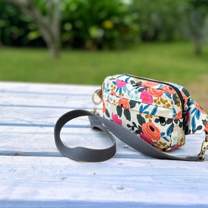 Puede incluir: Un peque&ntilde;o bolso bandolera de estampado floral con una correa ajustable gris. El bolso tiene una cremallera y un peque&ntilde;o bolsillo en la parte delantera.