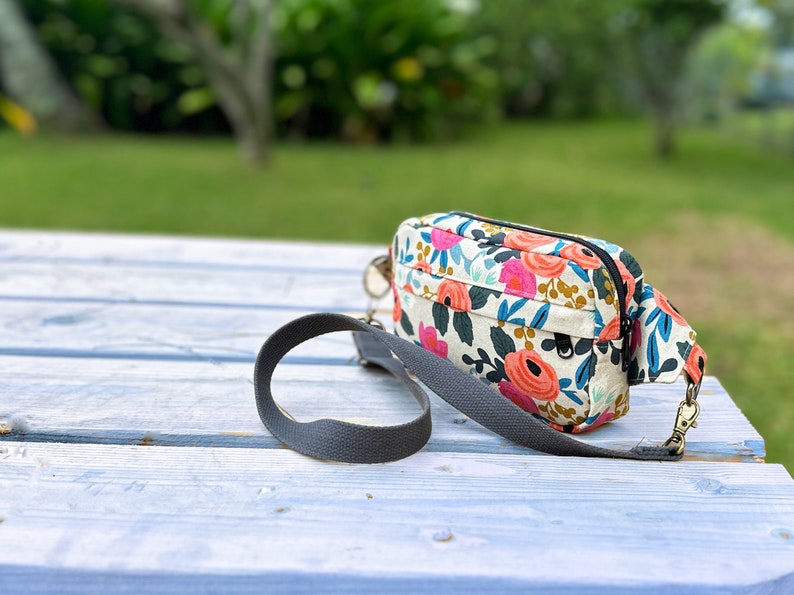 Puede incluir: Un peque&ntilde;o bolso bandolera de estampado floral con una correa ajustable gris. El bolso tiene una cremallera y un peque&ntilde;o bolsillo en la parte delantera.