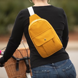 May include: A mustard yellow crossbody bag with a white strap and a zipper closure. The bag has a flap with a button closure and a small pocket on the front.