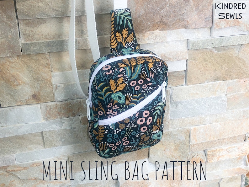 May include: A mini sling bag featuring a dark fabric with a colorful botanical print of leaves and flowers, a white diagonal zipper, and a white adjustable strap. The bag displays the text Kindred Sewls and Mini Sling Bag Pattern.