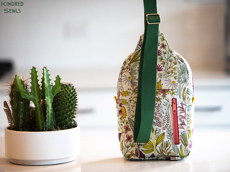 May include: A white and green floral print crossbody bag with a green adjustable strap. The bag has a zipper closure and a small pocket on the front.