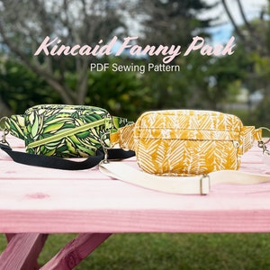 Puede incluir: Dos ri&ntilde;oneras, una verde con un patr&oacute;n de hojas y otra amarilla con un patr&oacute;n de hojas blancas, sobre una mesa de madera rosa. El texto "Kincaid Fanny Pack PDF Sewing Pattern" est&aacute; por encima de las ri&ntilde;oneras.