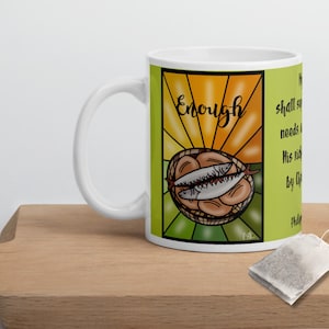 Può includere: Tazza in ceramica bianca con un'illustrazione colorata di un cesto di pane e pesce. Il testo "Enough" è al centro dell'immagine. Il testo "shall supply all your need according to his riches in glory by Christ Jesus" è sul lato destro della tazza.