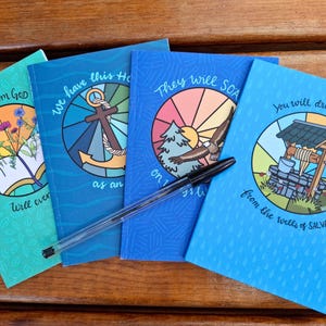 May include: Four notebooks with illustrations and text. The notebooks feature images of an open book with flowers, an anchor, an eagle, and a well. The text includes phrases like "no word from God" and "You will draw WATER". A pen rests across the notebooks.