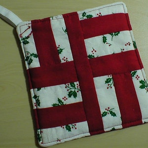 May include: Red and white quilted pot holder with a holly pattern. The pot holder has a loop for hanging.