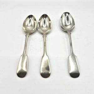 May include: Three silver spoons with oval bowls and long, slender handles. The spoons are arranged on a white surface, reflecting light. The spoons have a classic design, suitable for serving or display.