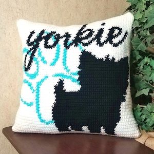 Pode incluir: Travesseiro branco de crochê com uma silhueta preta de um Yorkshire Terrier e a palavra "yokie" em letras cursivas pretas.